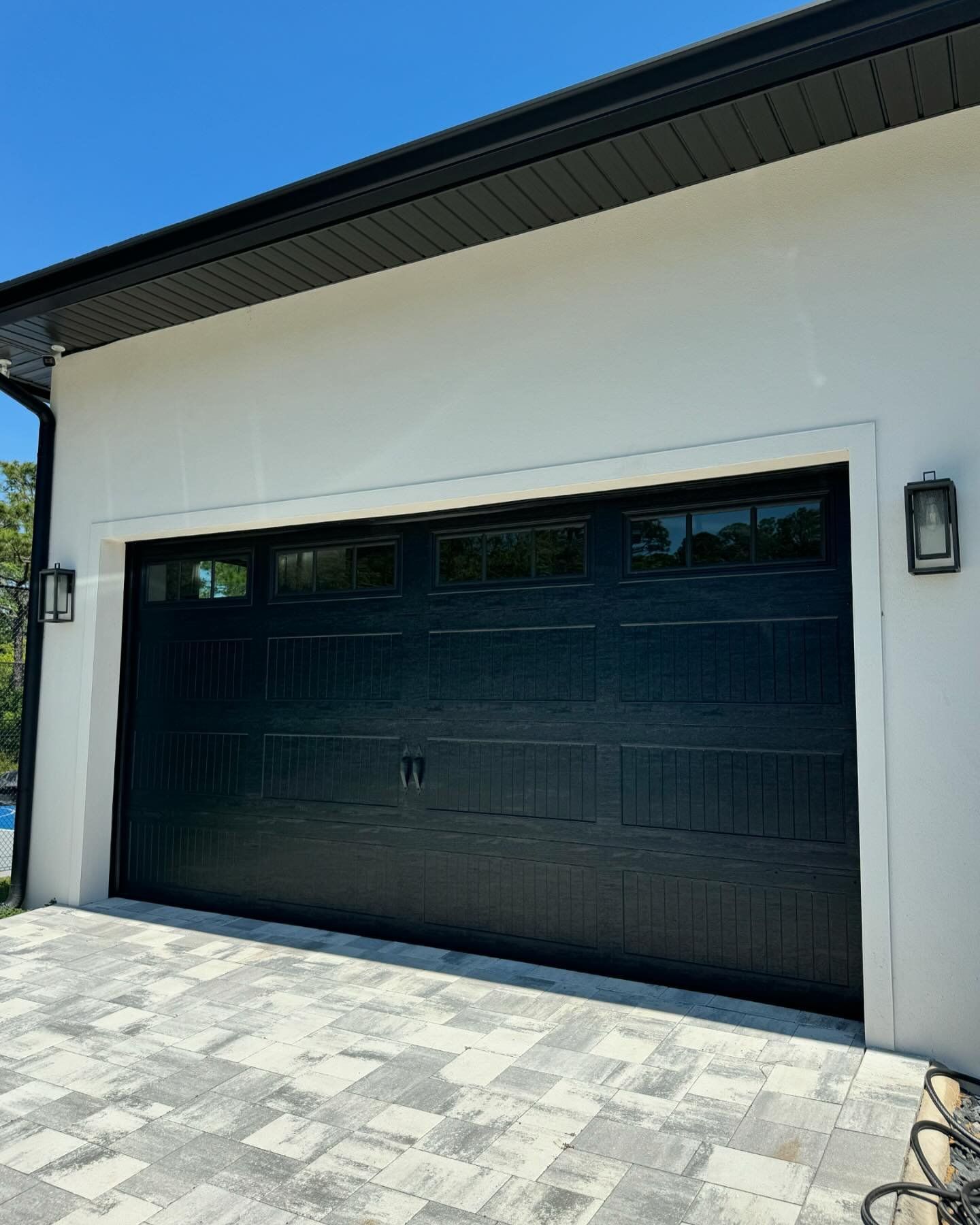 A black garage door is on the side of a white house.