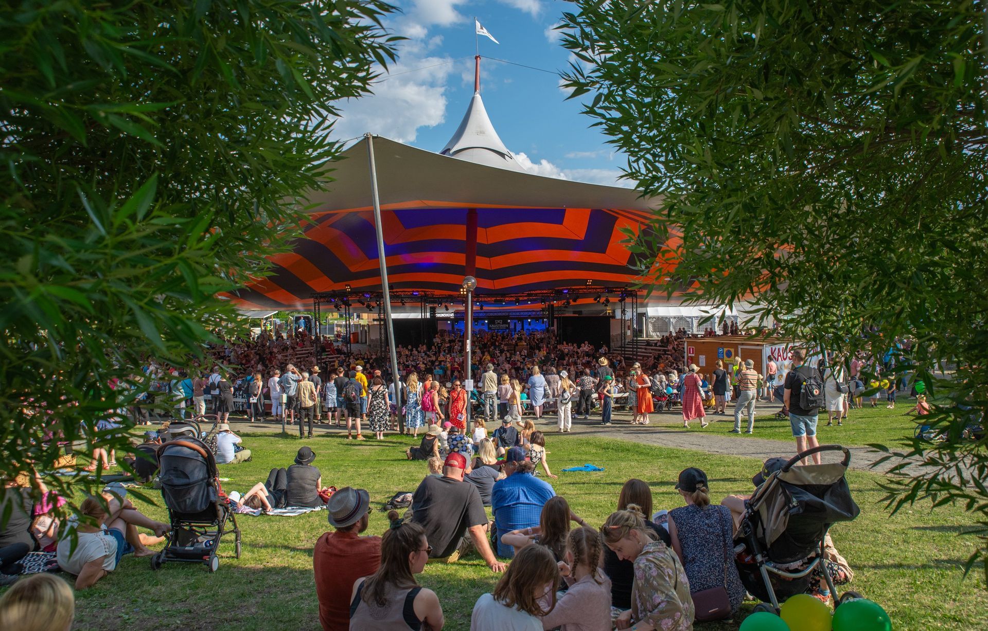 a group of people are sitting in the grass under a tent at a concert .