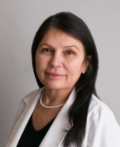 Portrait of a woman in a white coat and pearl necklace against a gray background