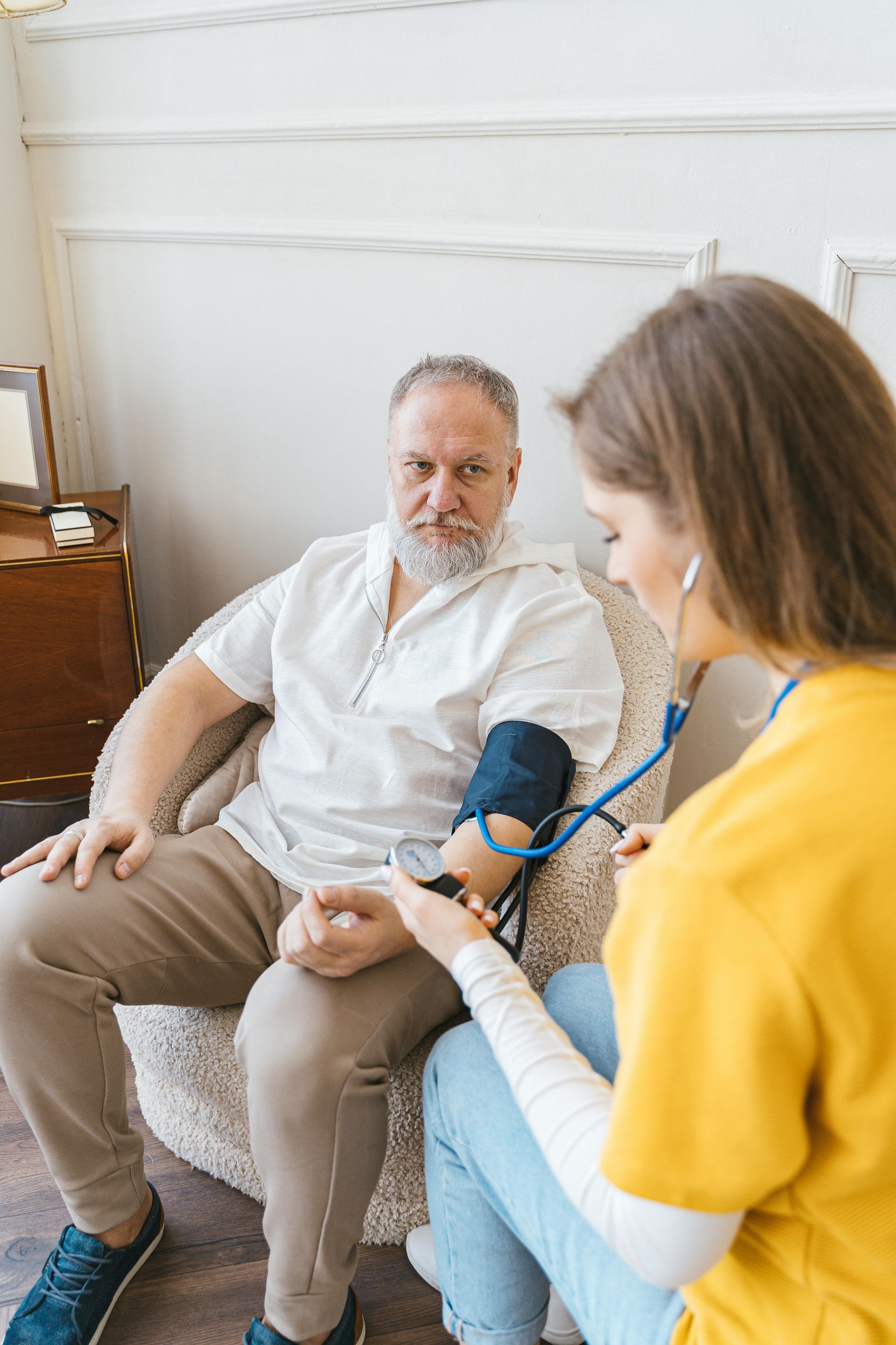 Health worker checking an older man’s blood pressure in a living room