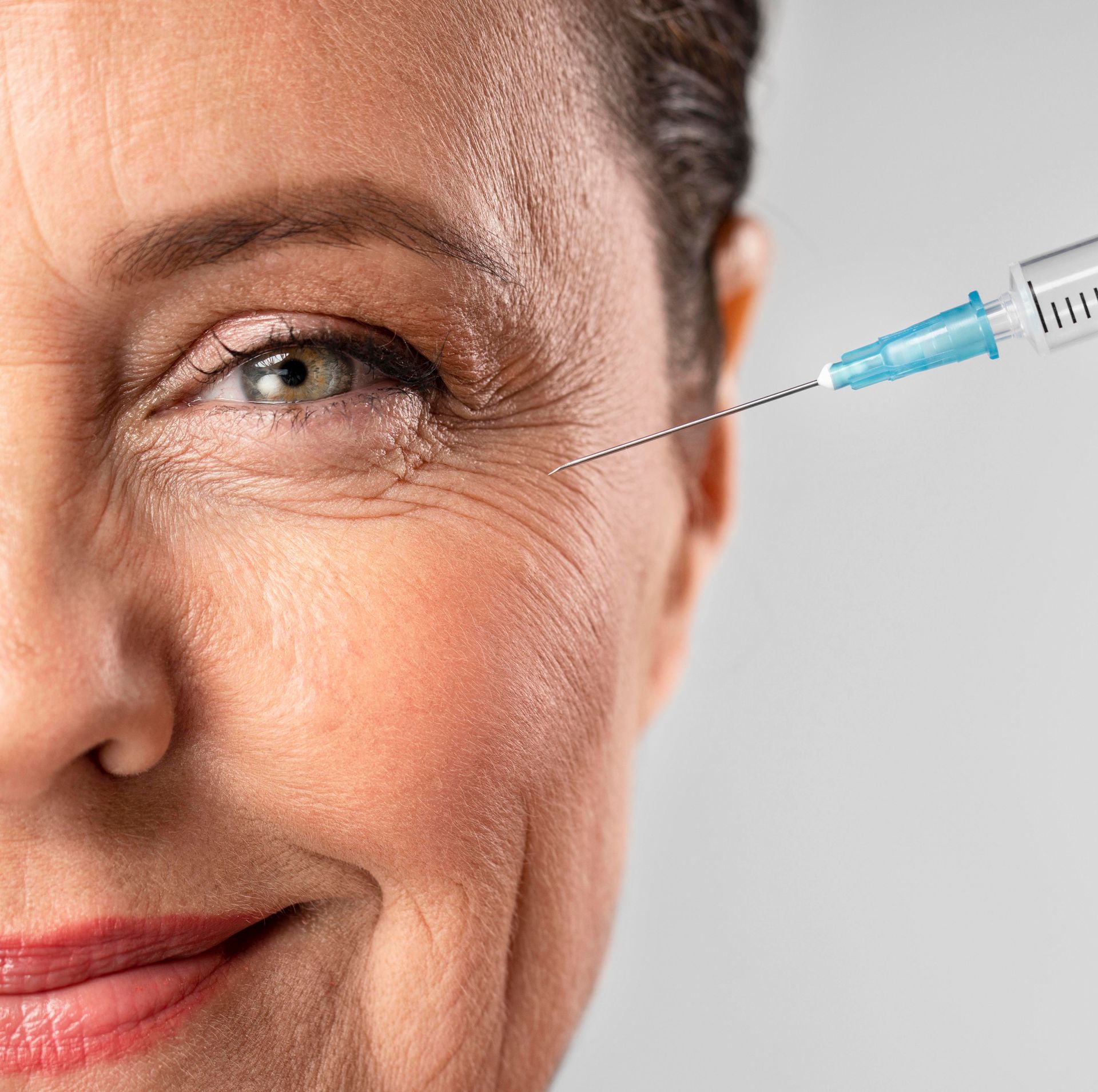 Close-up of a woman's face with a syringe near her eye, suggesting a cosmetic injection
