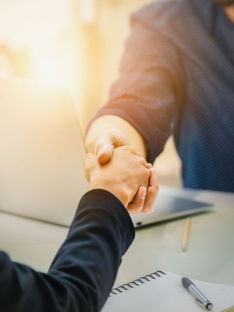 A man and a woman are shaking hands in front of a laptop.