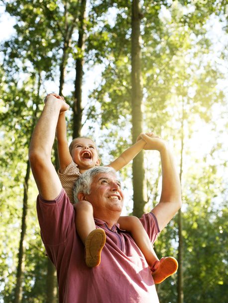 A man is carrying a baby on his shoulders in the woods.