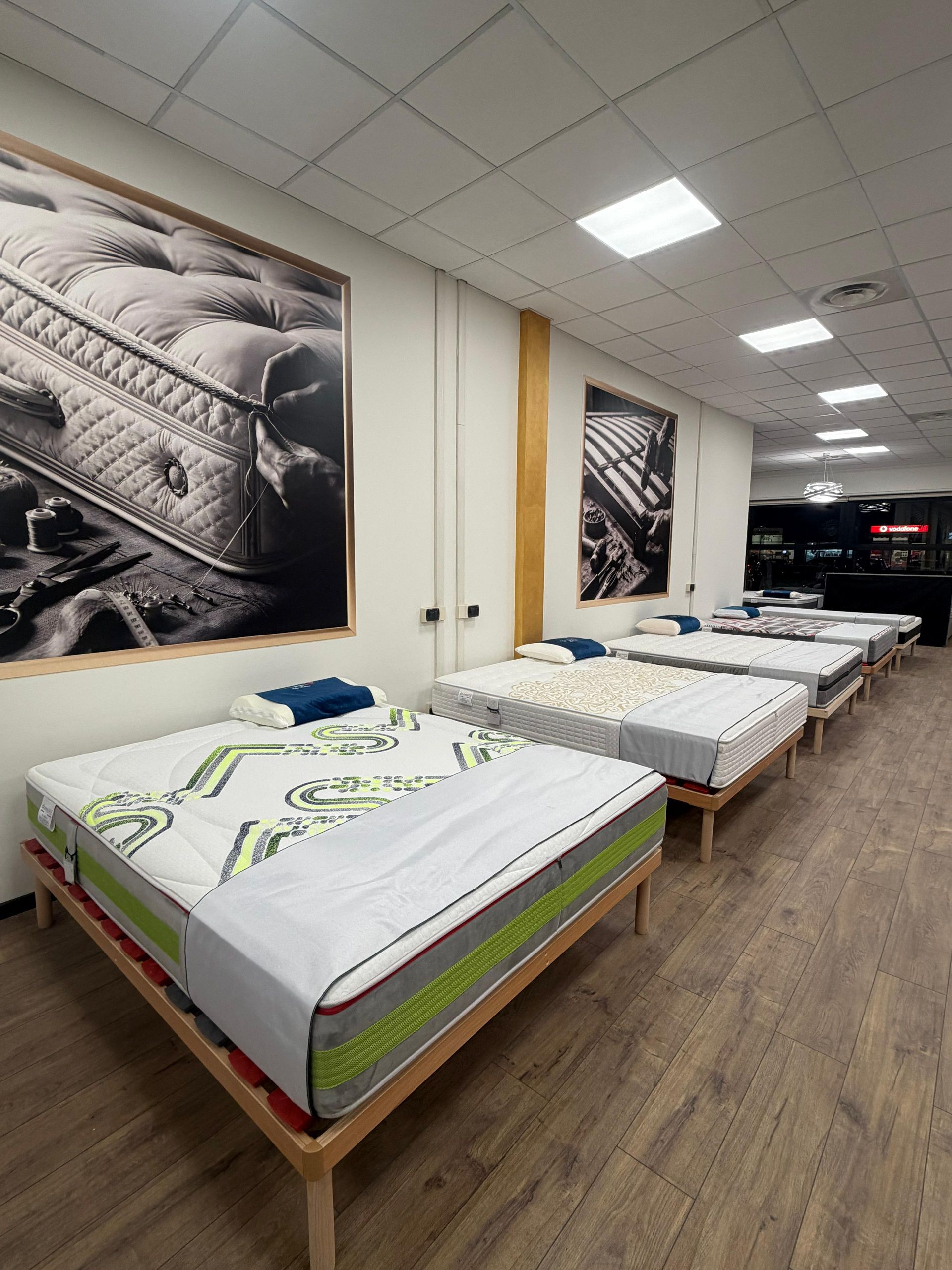 Showroom di materassi con numerosi letti esposti; quadri incorniciati alle pareti.