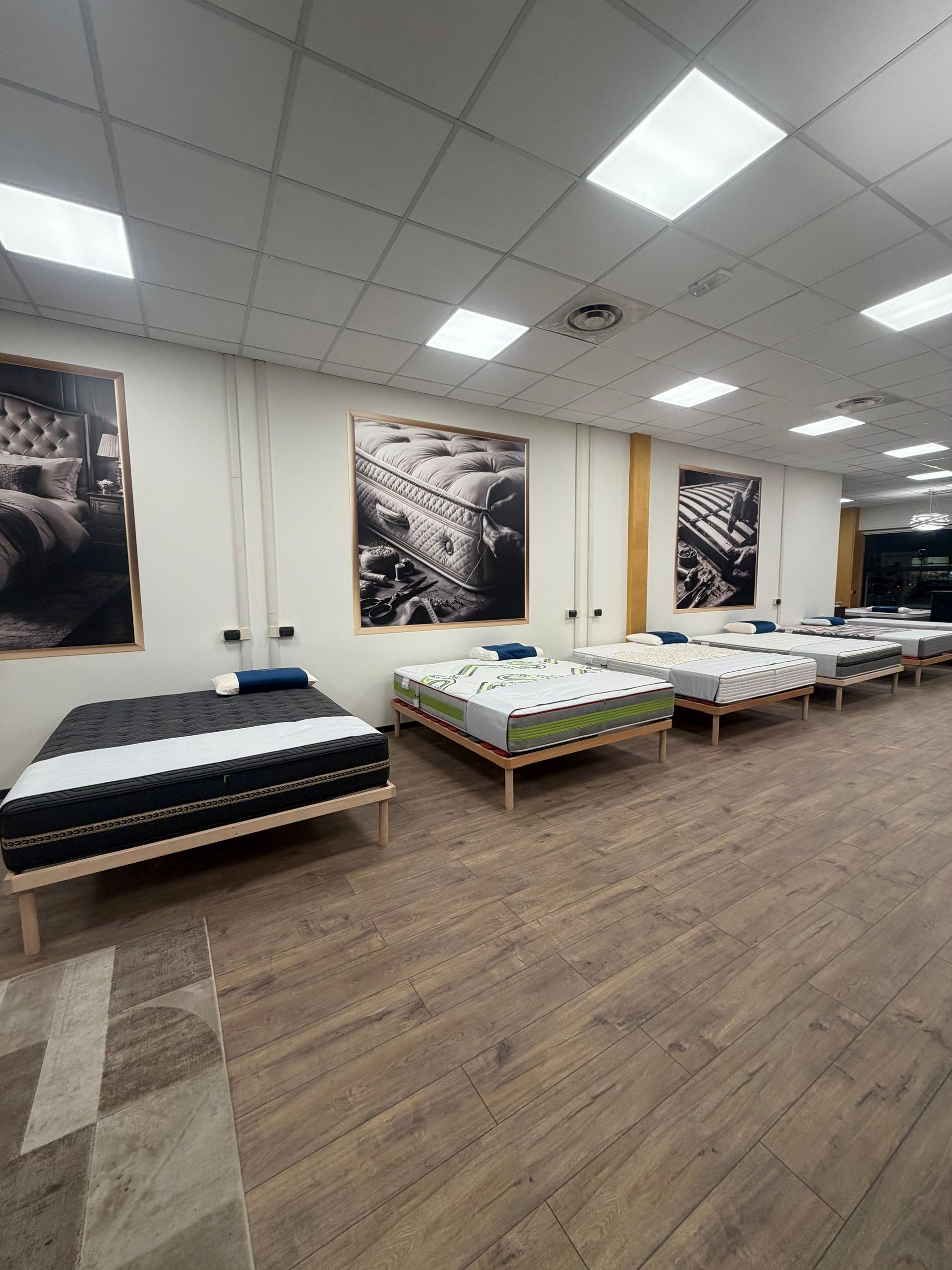 Materassi esposti in un negozio, pavimenti in legno, pareti bianche con grandi quadri, luci da incasso.