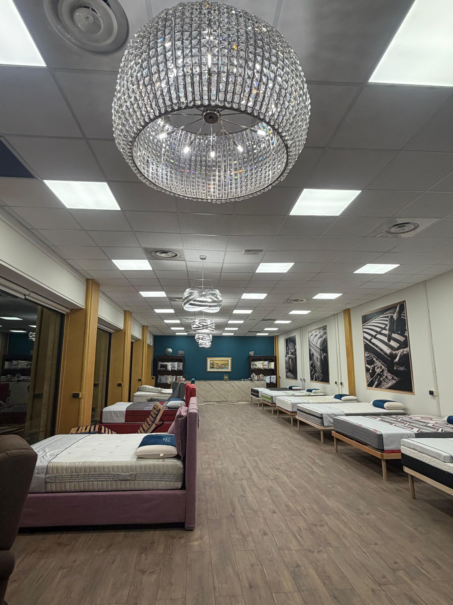 Uno showroom con materassi in esposizione; un grande lampadario di cristallo pende dal soffitto.