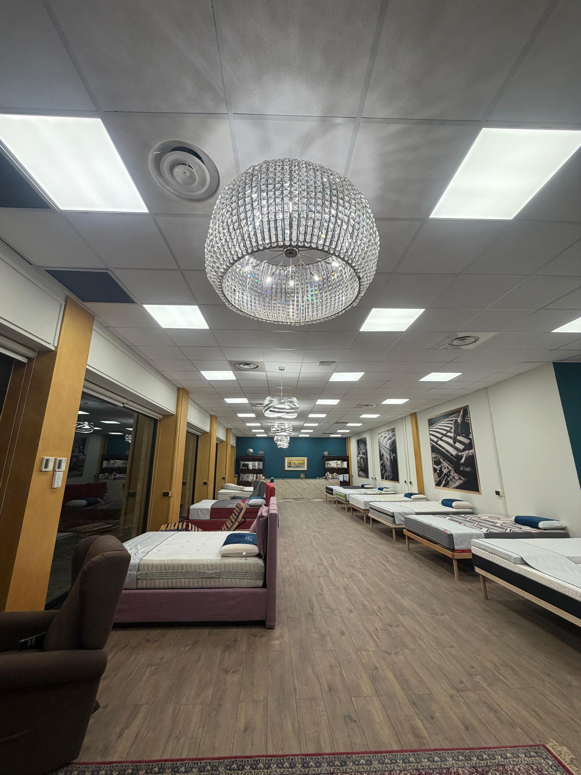 Interno di un negozio di materassi con lampadari, numerosi letti esposti e un lungo corridoio.