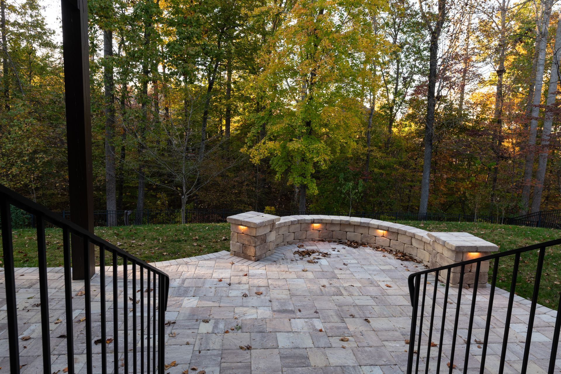 Stone patio with curved wall, railing, and trees in background.