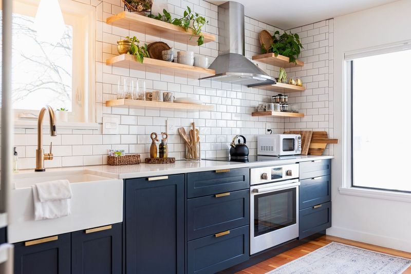 A kitchen with blue cabinets , stainless steel appliances , a sink , and a window.