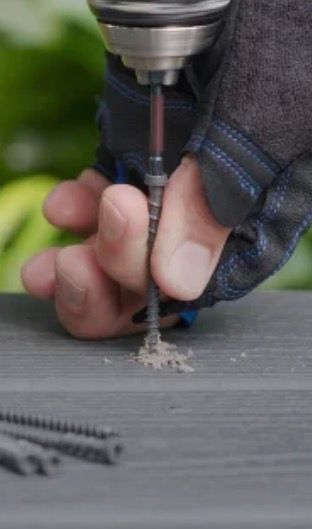 Hand drilling a hole into gray wood; gray gloves worn.