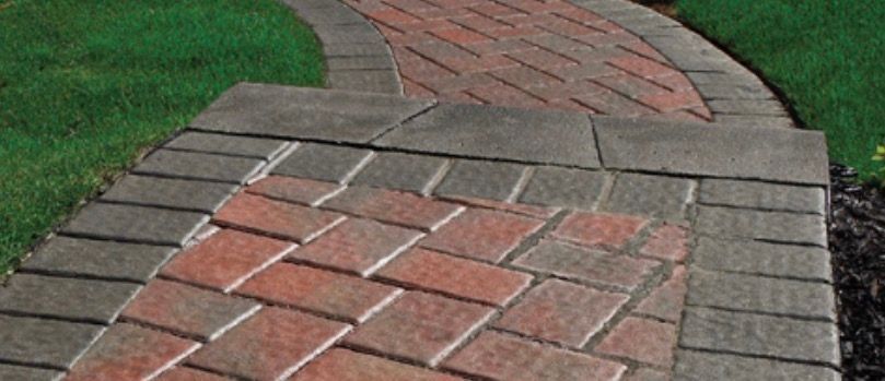 A brick pathway with a grass border, leading up to a step with a contrasting brick pattern.