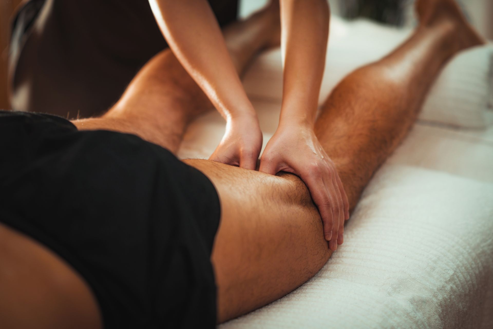 A physical therapist in a blue shirt performs a leg stretch on a patient lying on a treatment table in a gym.