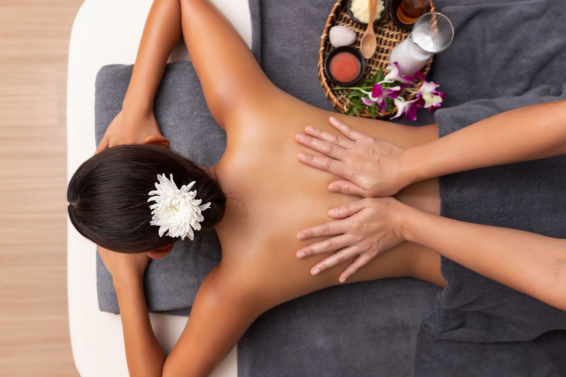 Top view of a person receiving a back massage on a gray towel, with a small tray of spa accessories nearby.