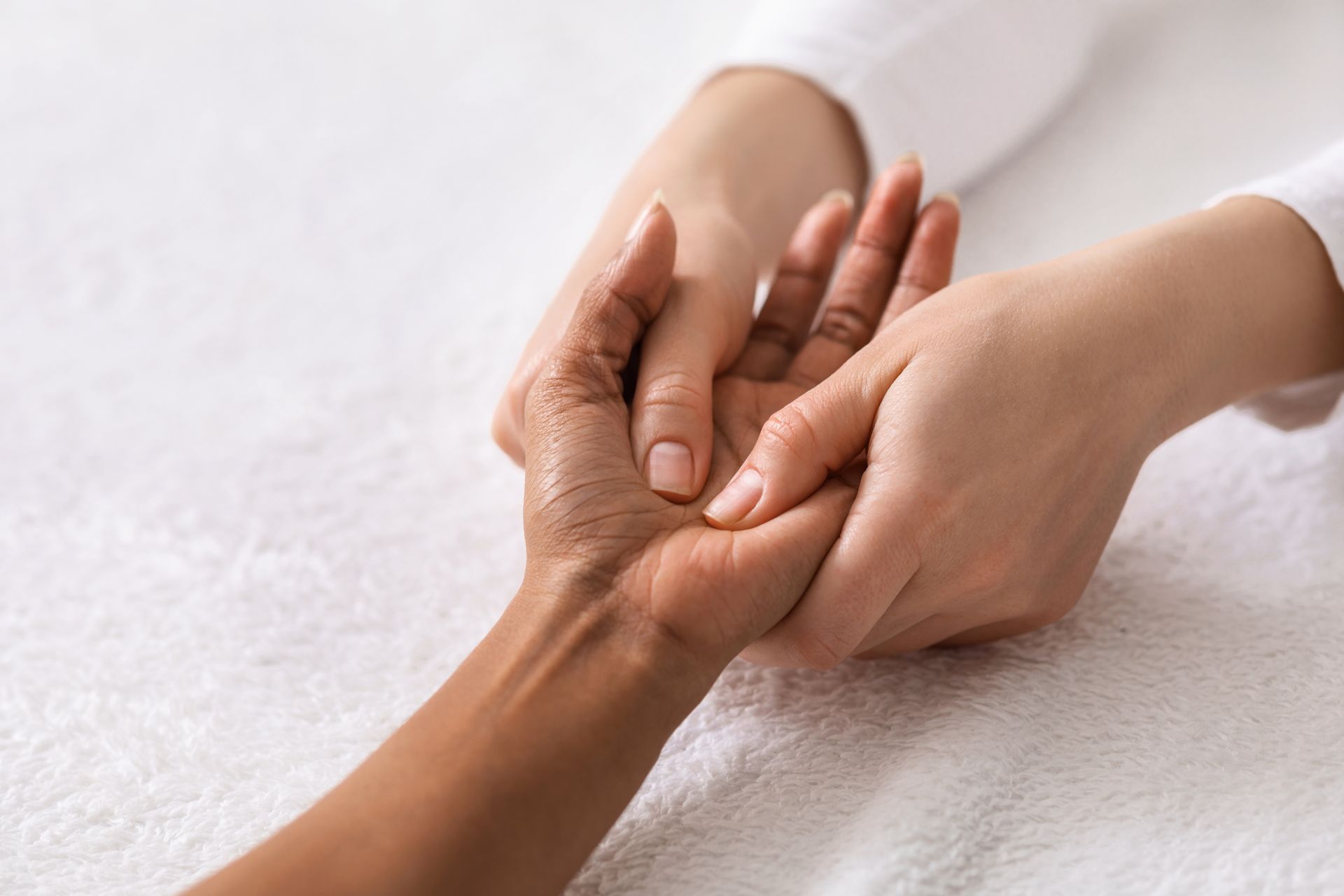 A person’s hands gently massaging the palm of another person’s hand over a white, textured surface.