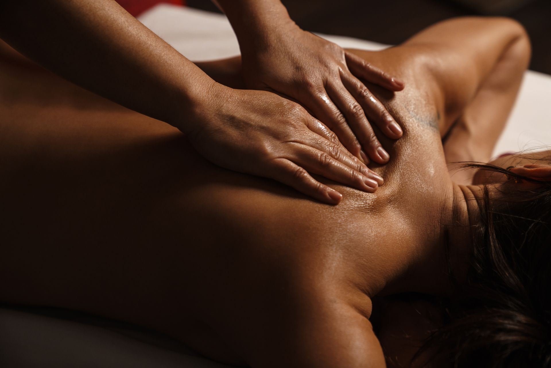 A person receiving a massage while lying on their stomach, with hands applying pressure to their upper back.