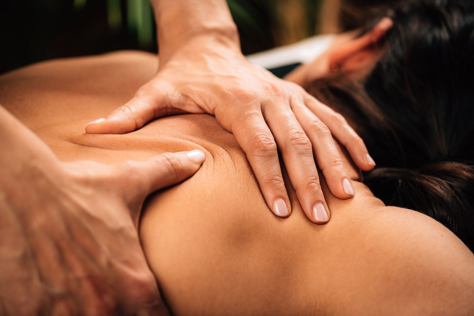 Hands perform a professional massage on a person's upper back and shoulder area.
