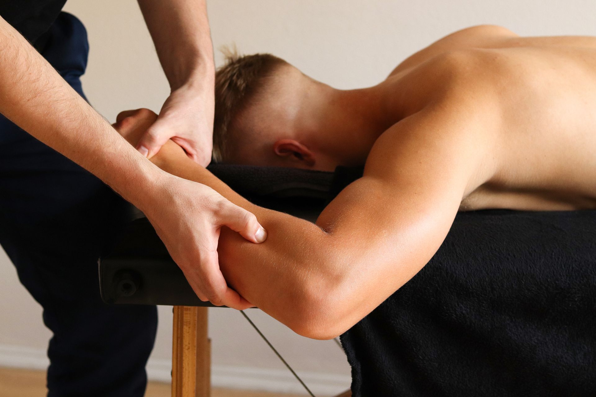 A physical therapist in a blue shirt performs a leg stretch on a patient lying on a therapy table in a blue room.