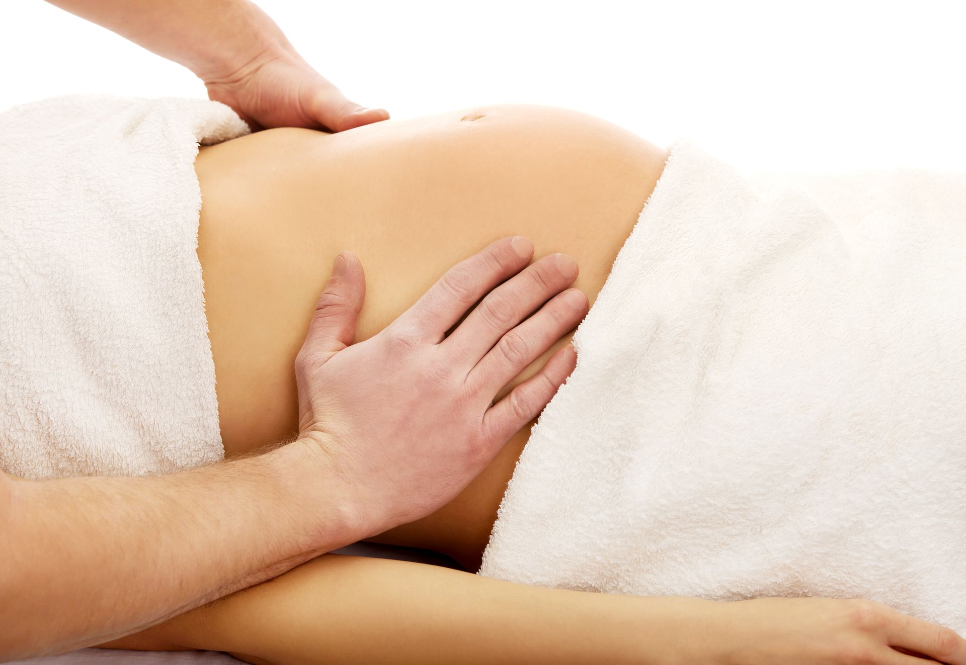 A person's hands gently massage a pregnant abdomen covered by white towels.