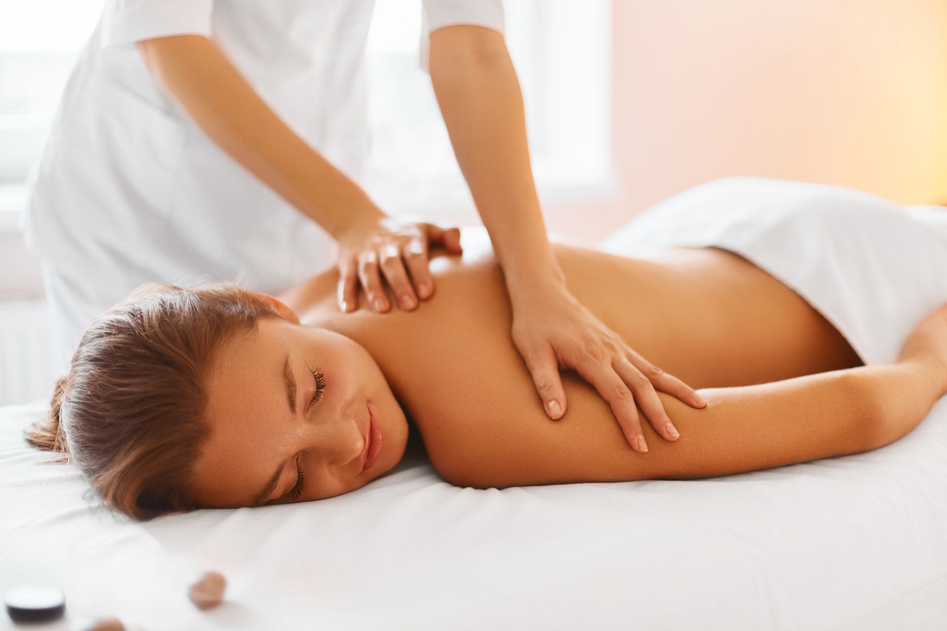 A professional massage therapist provides a back massage to a person lying on a table with their eyes closed in relaxation.