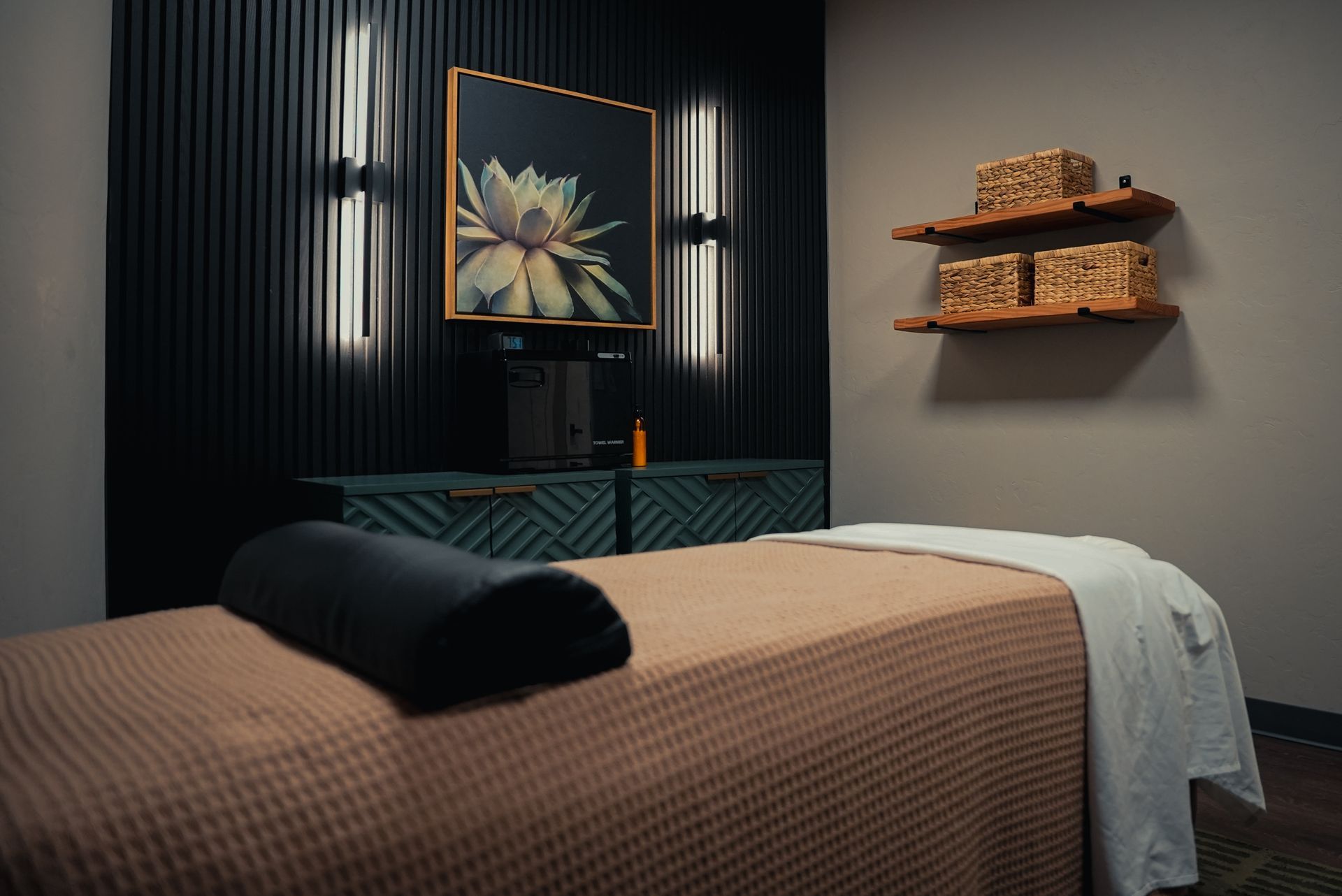 Modern rooms with massage tables, textured wall panels with recessed lighting, wooden slats, and potted greenery.