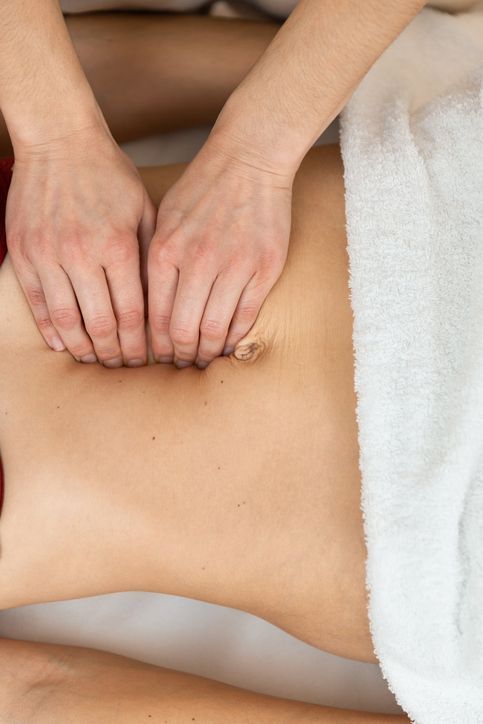 A pair of hands performs a massage on a person's abdomen, partially covered by a white towel.