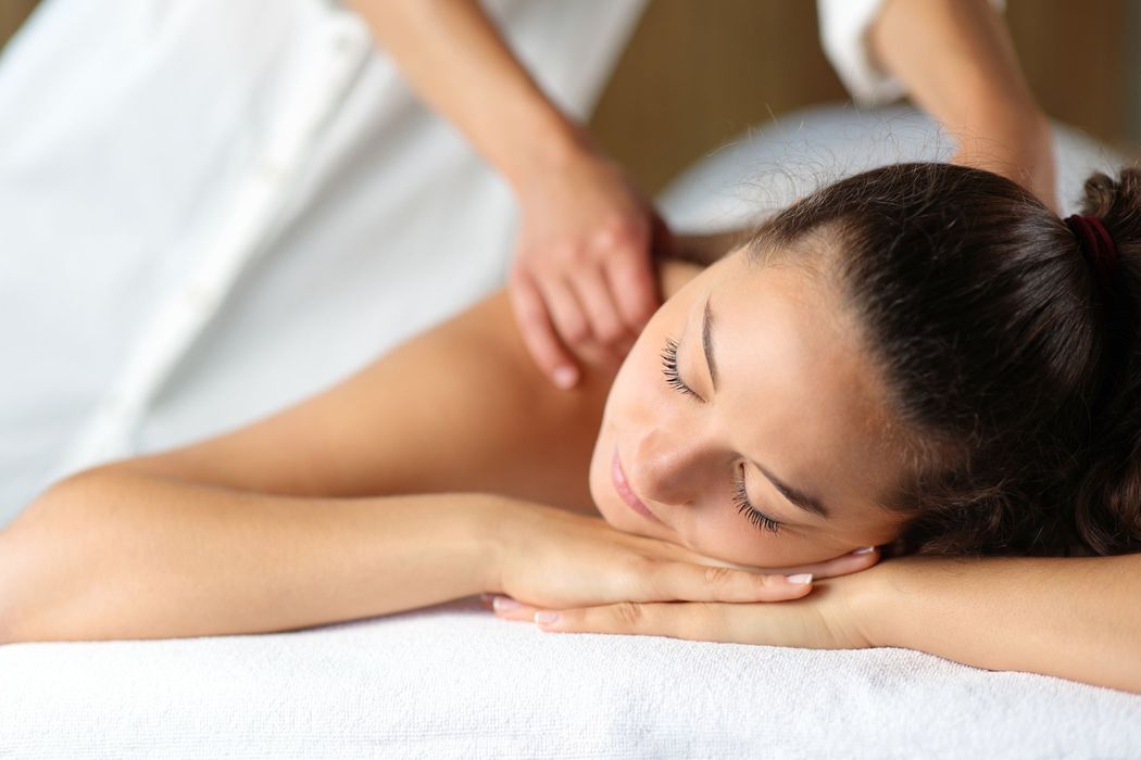 A person lying on a white surface with their eyes closed while receiving a massage on their shoulders. A person lying on a white surface with their eyes closed while receiving a massage on their shoulders.