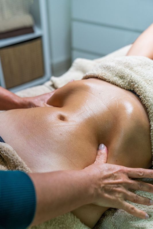 A professional therapist performs a lymphatic drainage massage on a person's abdomen in a massage setting. A professional therapist performs a lymphatic drainage massage on a person's abdomen in a massage setting.