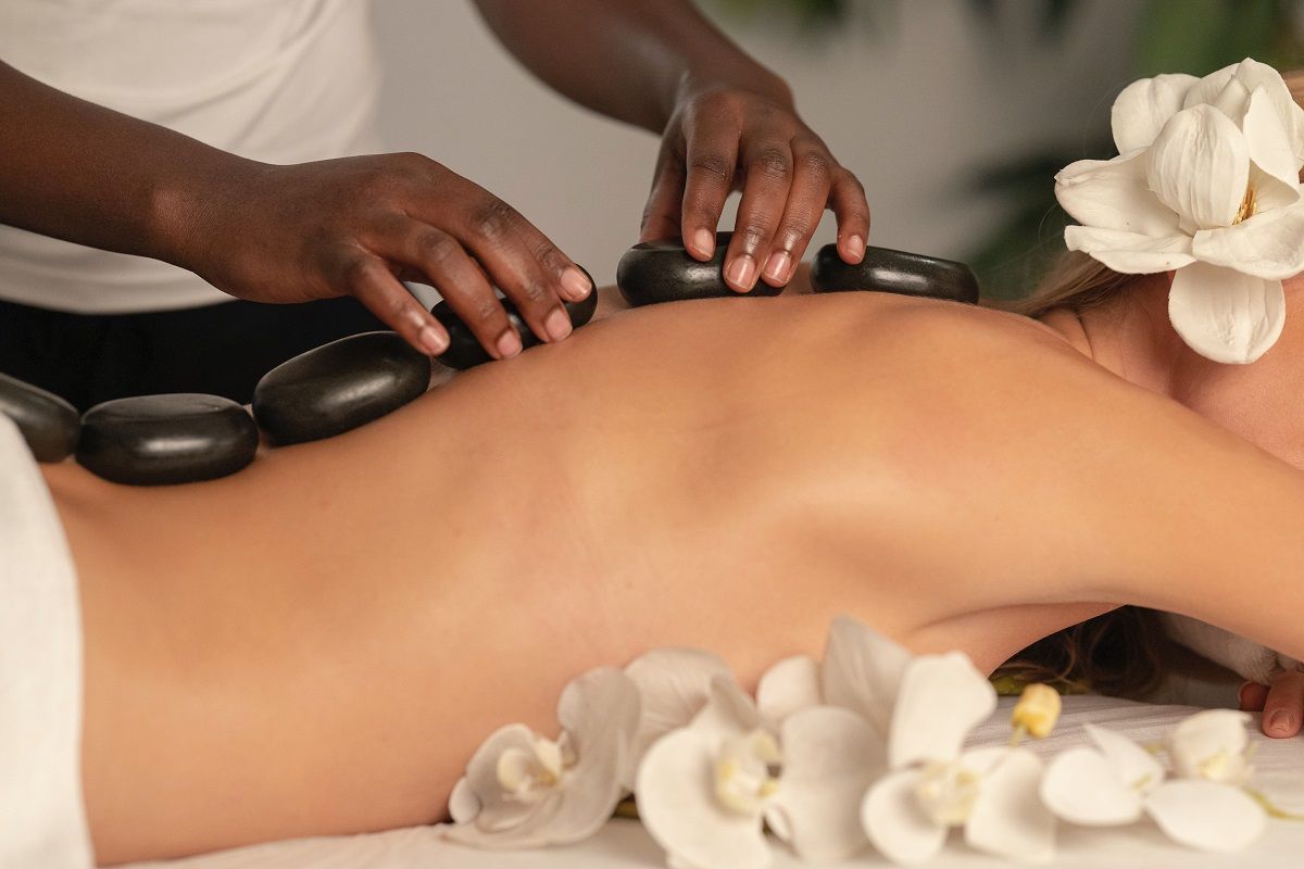 A person receiving a hot stone massage while lying on a table adorned with white orchids.