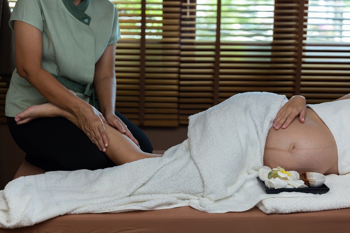 A massage therapist performs a leg massage on a pregnant person lying on a treatment table in a spa.