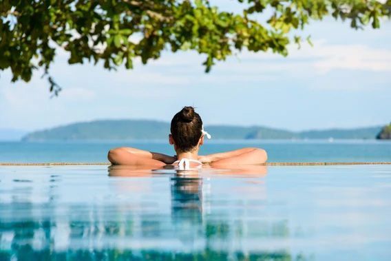 A person rests their arms on the edge of an infinity pool overlooking a tropical ocean and distant islands.