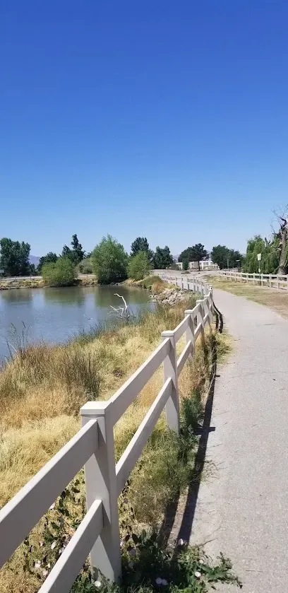 A white fence along a path next to a lake.