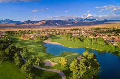 An aerial view of a golf course with a lake and mountains in the background.