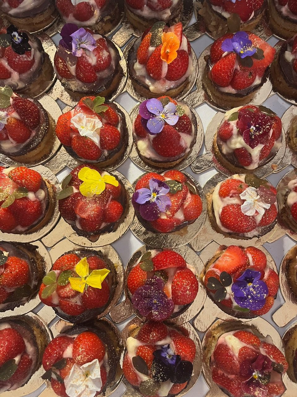 En masse individuele små kager med jordbær og spiselige blomster på.