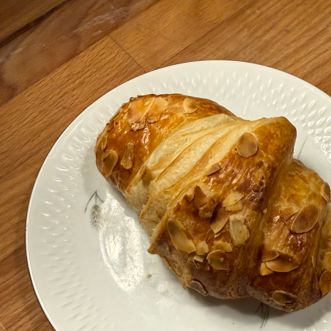 Gylden mandelcroissant på en hvid tallerken på et træbord