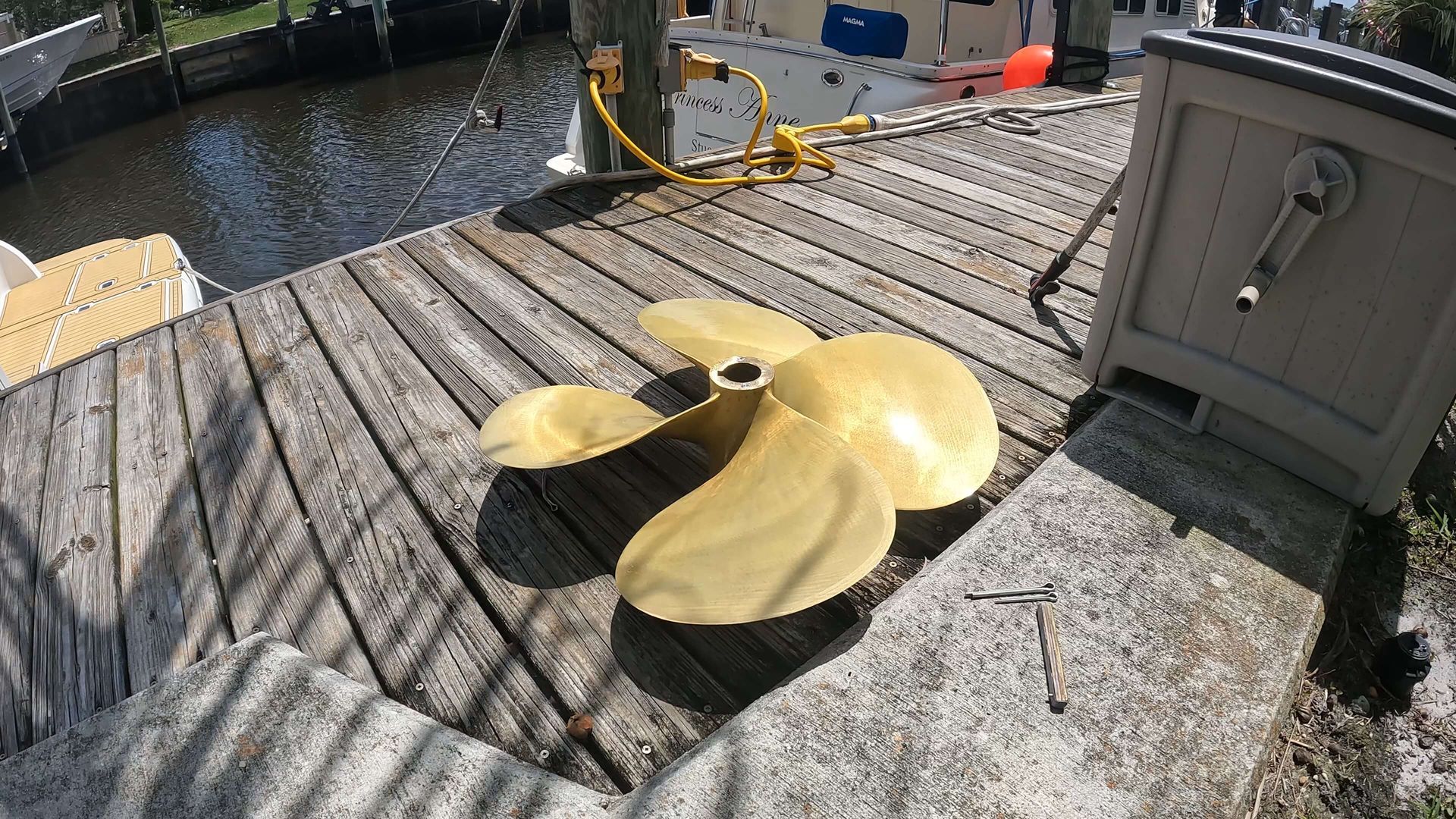 A brass propeller is sitting on a wooden deck next to a boat.