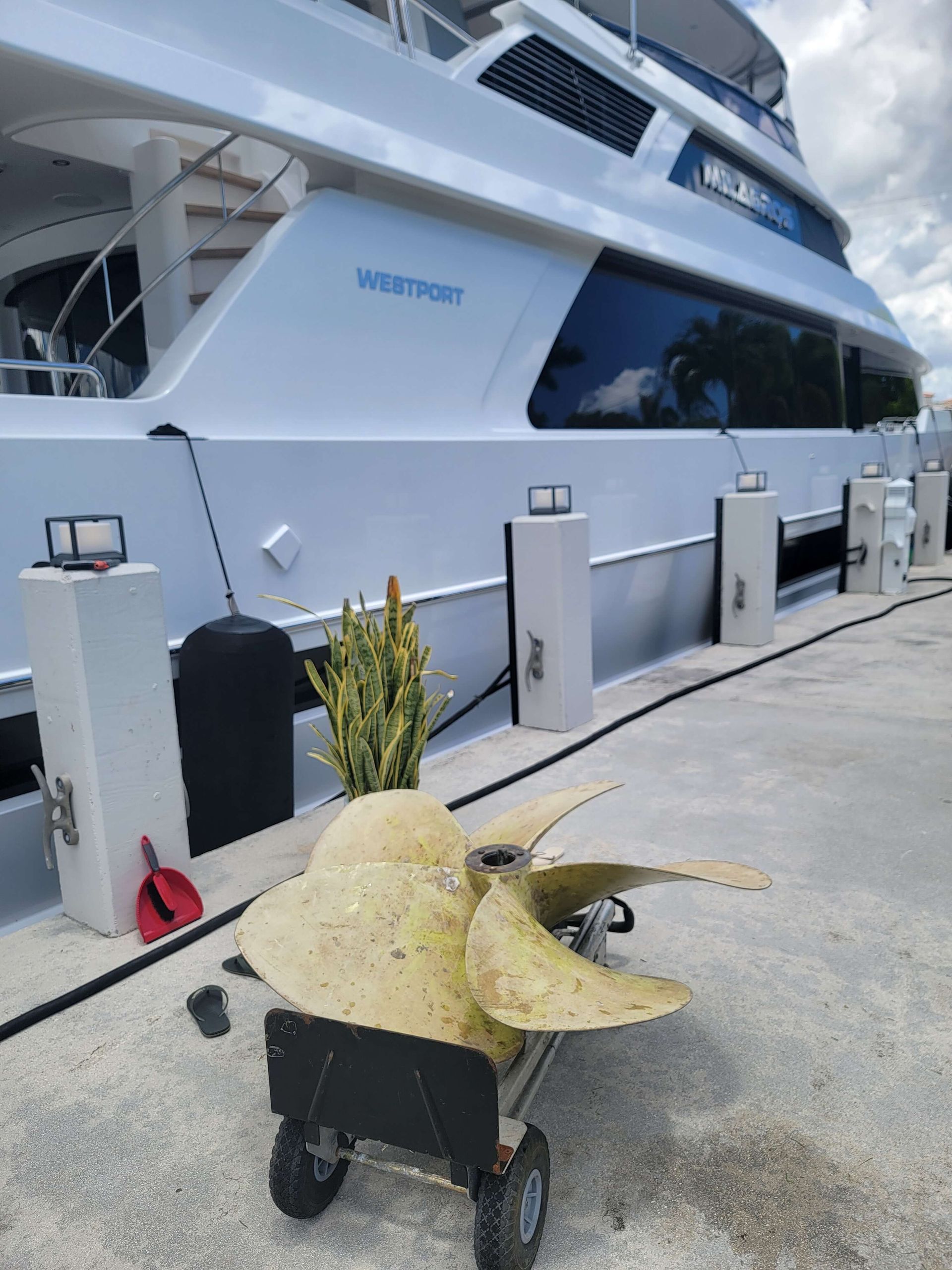 A large propeller is on a cart in front of a large boat