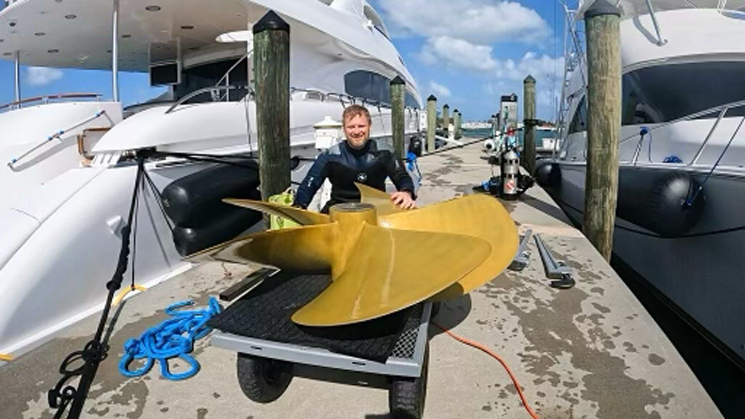 A man is holding a large propeller in front of a boat.