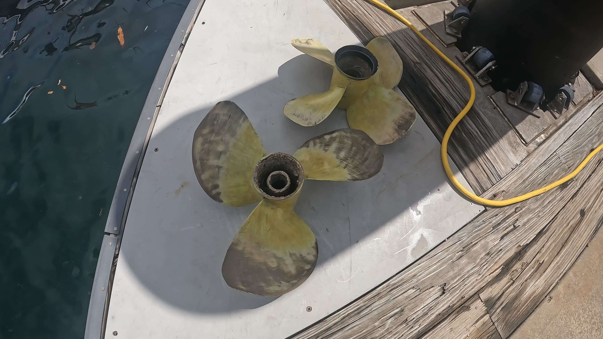Two propellers are sitting on a wooden deck next to a yellow cord