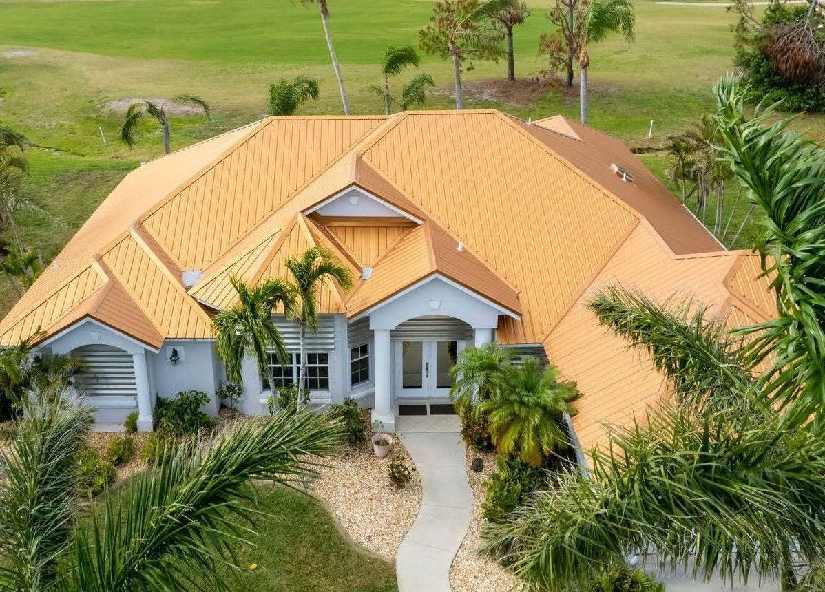 A light blue house with orange roof, palm trees. Walkway leading to the front door.