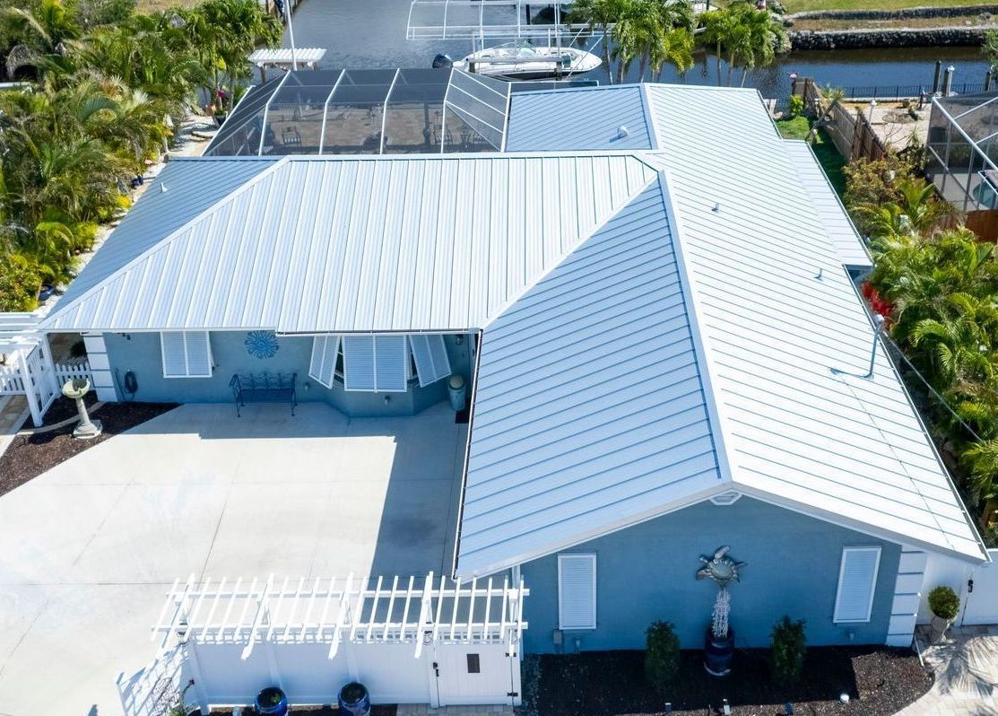 Aerial view of a blue house with white metal roof and shutters, in a tropical setting.