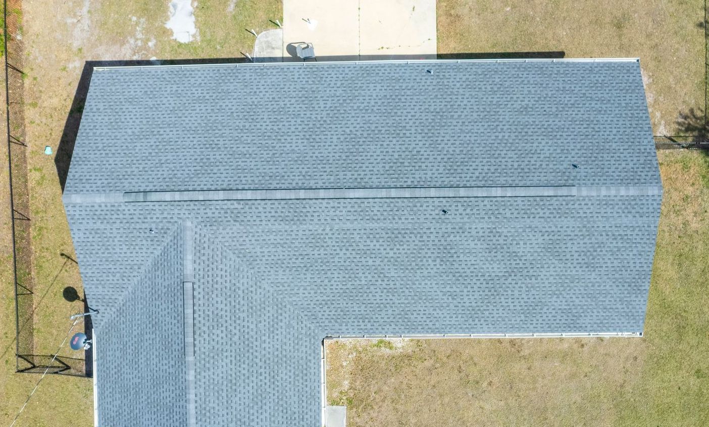 Overhead view of a house with a dark gray shingle roof. The house is surrounded by green grass and a fence.