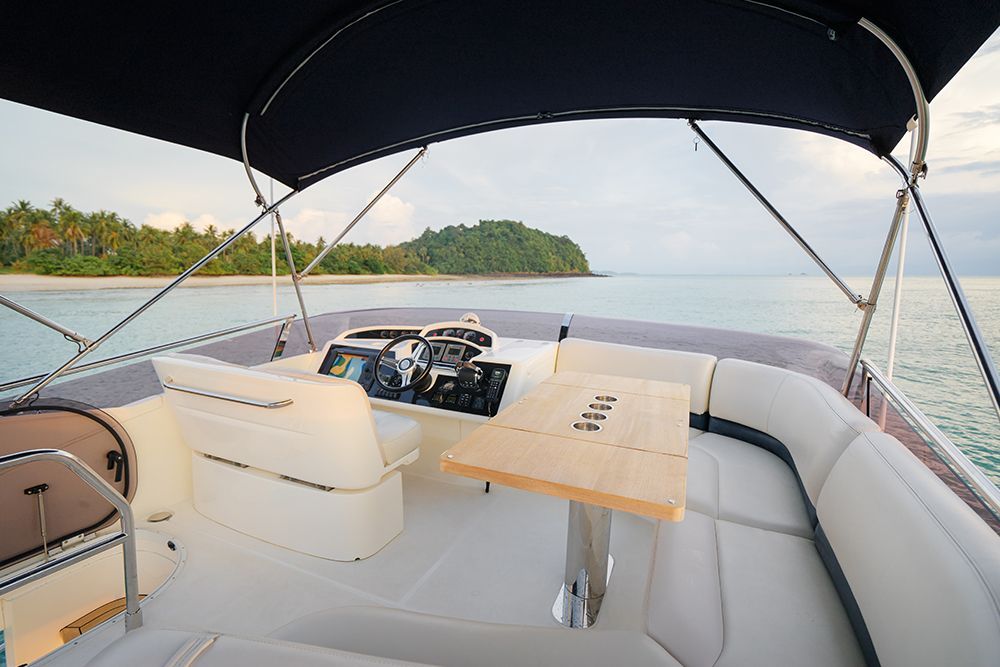 View from a boat deck towards a tropical island, with a table, helm, and canopy.