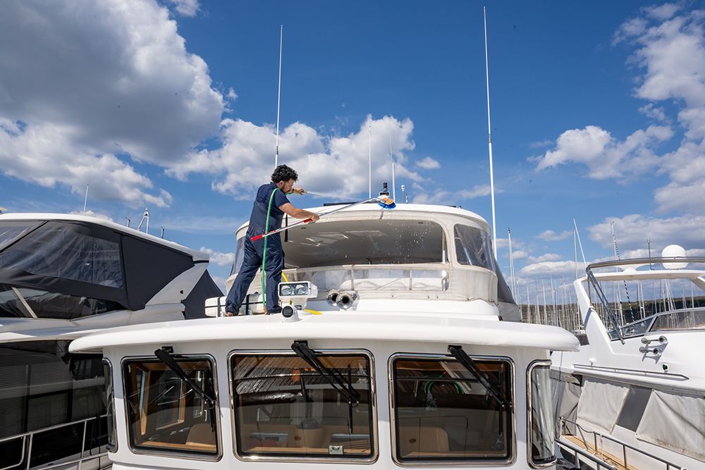 A person on boat roof cleaning the windshield. Blue jumpsuit, sunny day, marina.