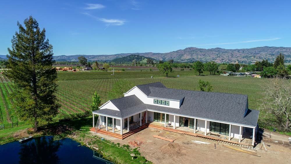 An aerial view of a house in a vineyard with mountains in the background.