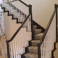 A man is standing on a ladder painting a staircase.