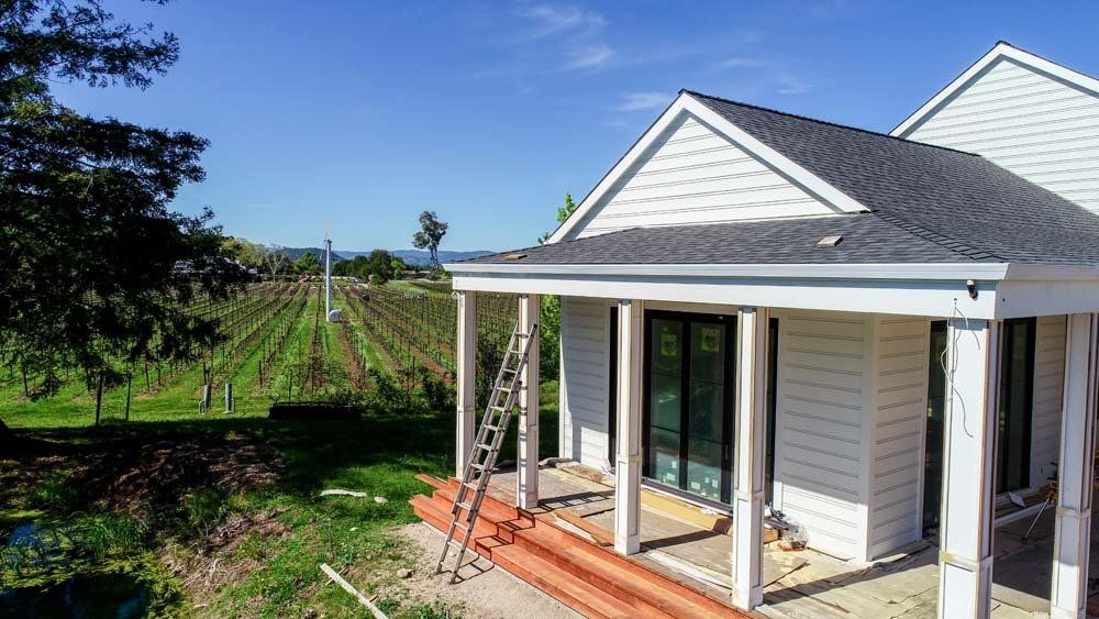 A white house with a porch and a ladder in front of it.