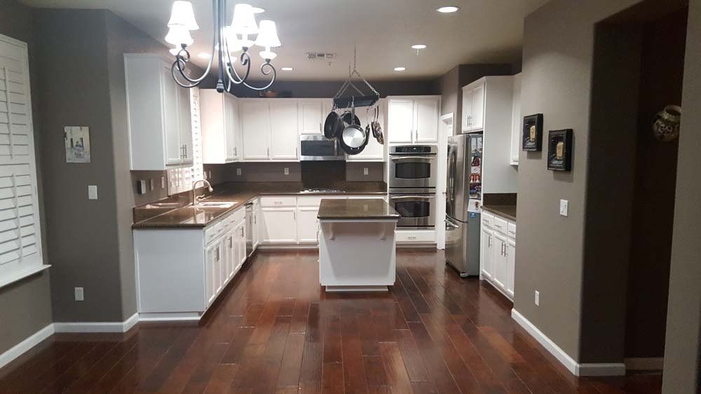 A kitchen with hardwood floors , white cabinets , stainless steel appliances and a large island.