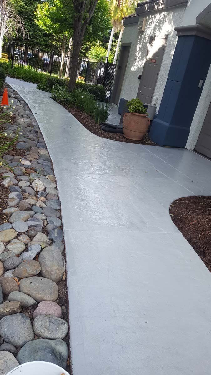 A concrete walkway leading to a house with rocks on the side.