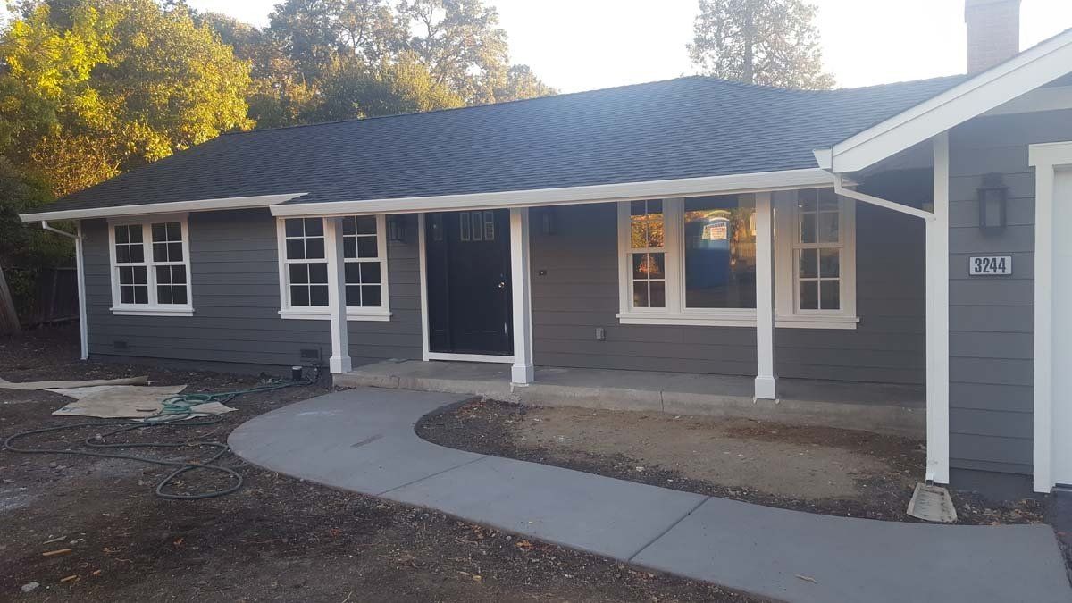 A gray house with a white porch and a walkway leading to it.