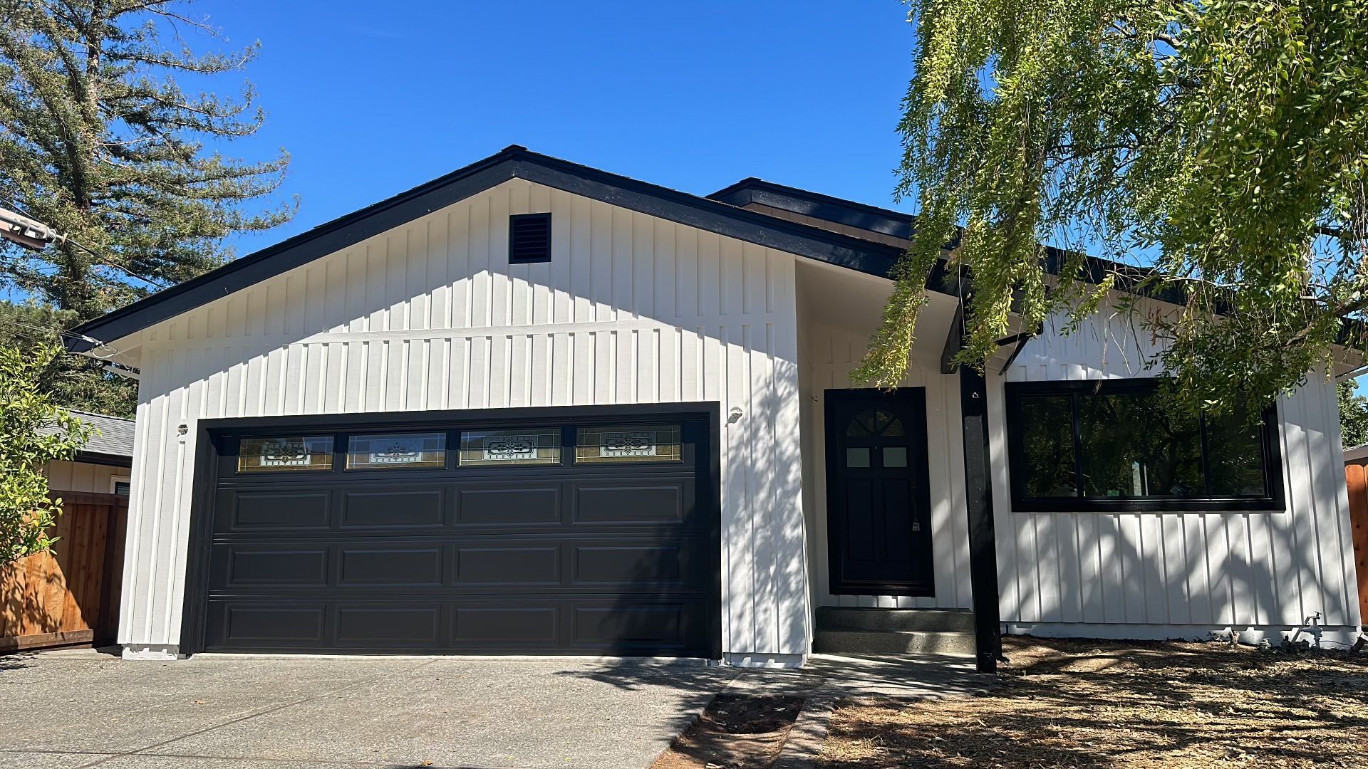 A white house with a black garage door and a tree in front of it.